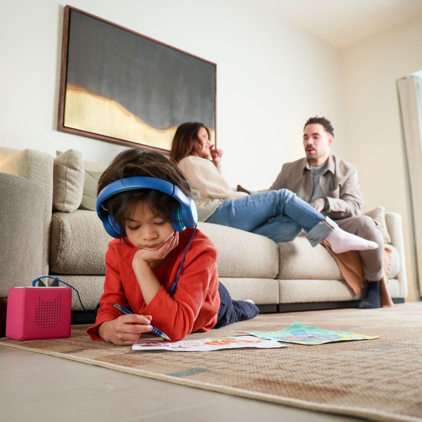 Child wearing headphones drawing pictures on the rug with parents sitting on the sofa talking in the background