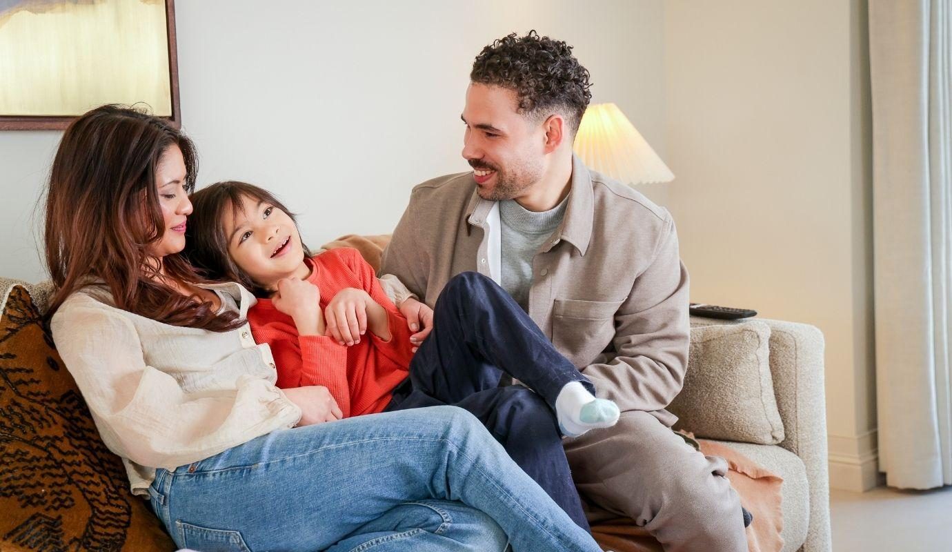 Man woman and child smiling and embracing on living room sofa