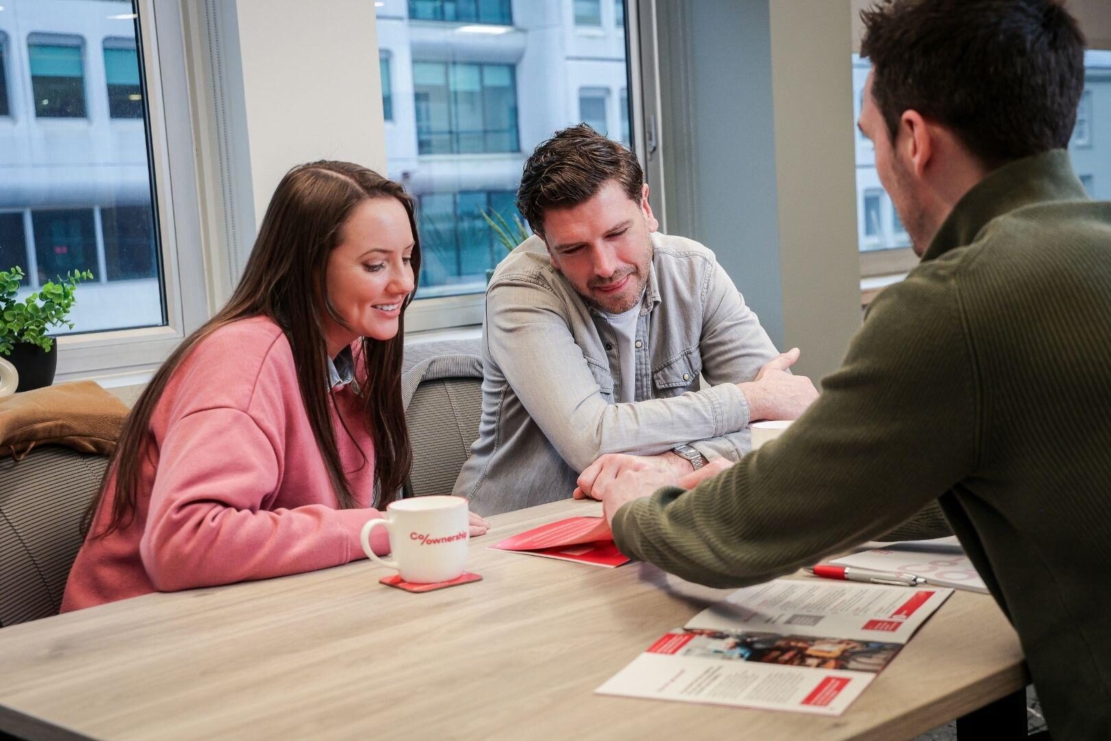 Man pointing to pages in brochure sitting with couple at table