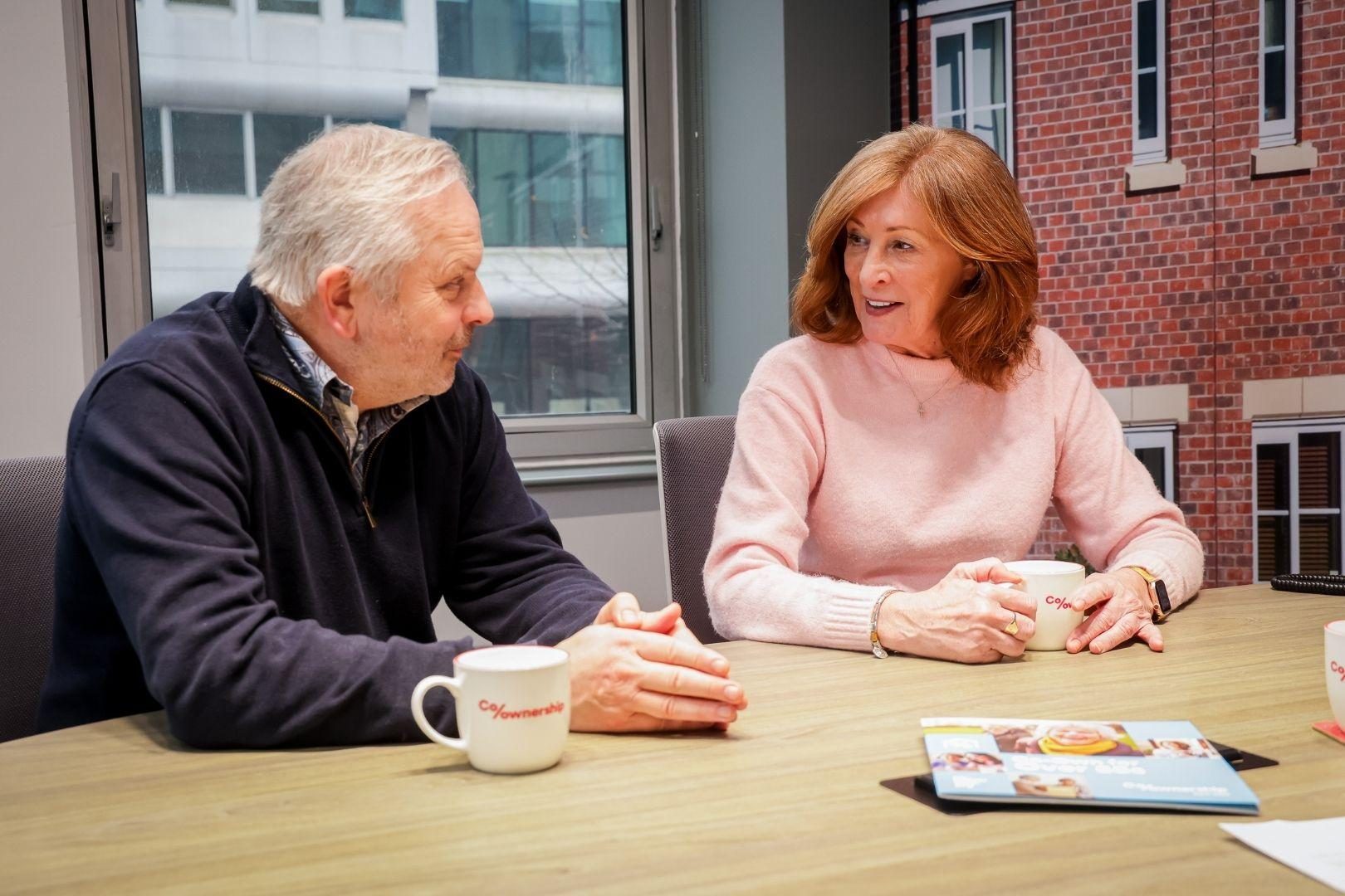 Man and woman sitting at table with branded mugs having a conversation