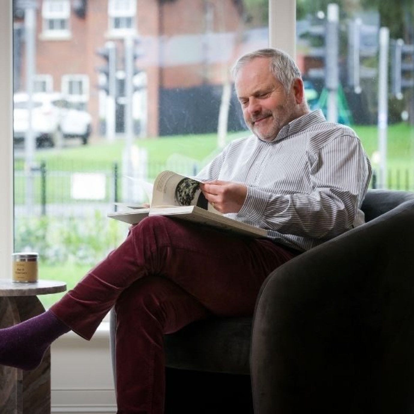 Man turning page of book sitting in living room armchair by big window