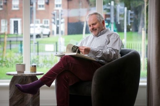 Man turning page of book sitting in living room armchair by big window