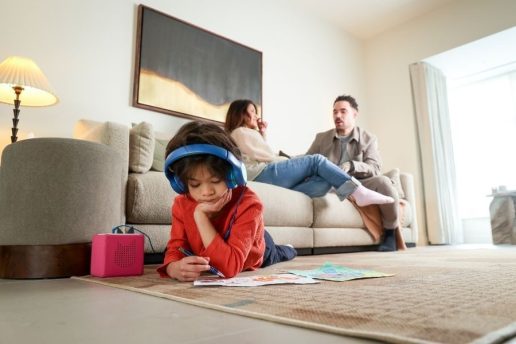 Child wearing headphones drawing pictures on the rug with parents sitting on the sofa talking in the background